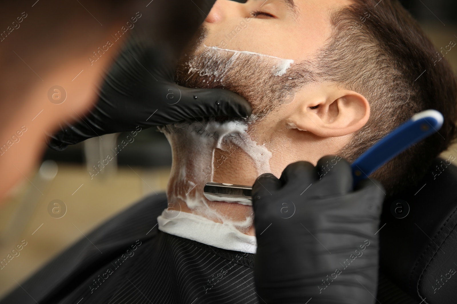 Photo of Professional hairdresser shaving client with straight razor in barbershop