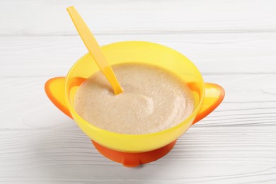Photo of Baby food. Puree and spoon in bowl on white wooden table