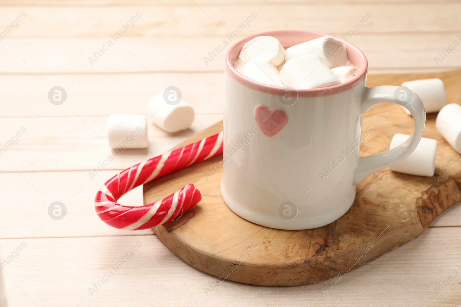 Photo of Tasty hot chocolate with marshmallows and candy cane on light wooden table, closeup