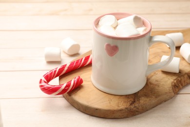 Photo of Tasty hot chocolate with marshmallows and candy cane on light wooden table, closeup