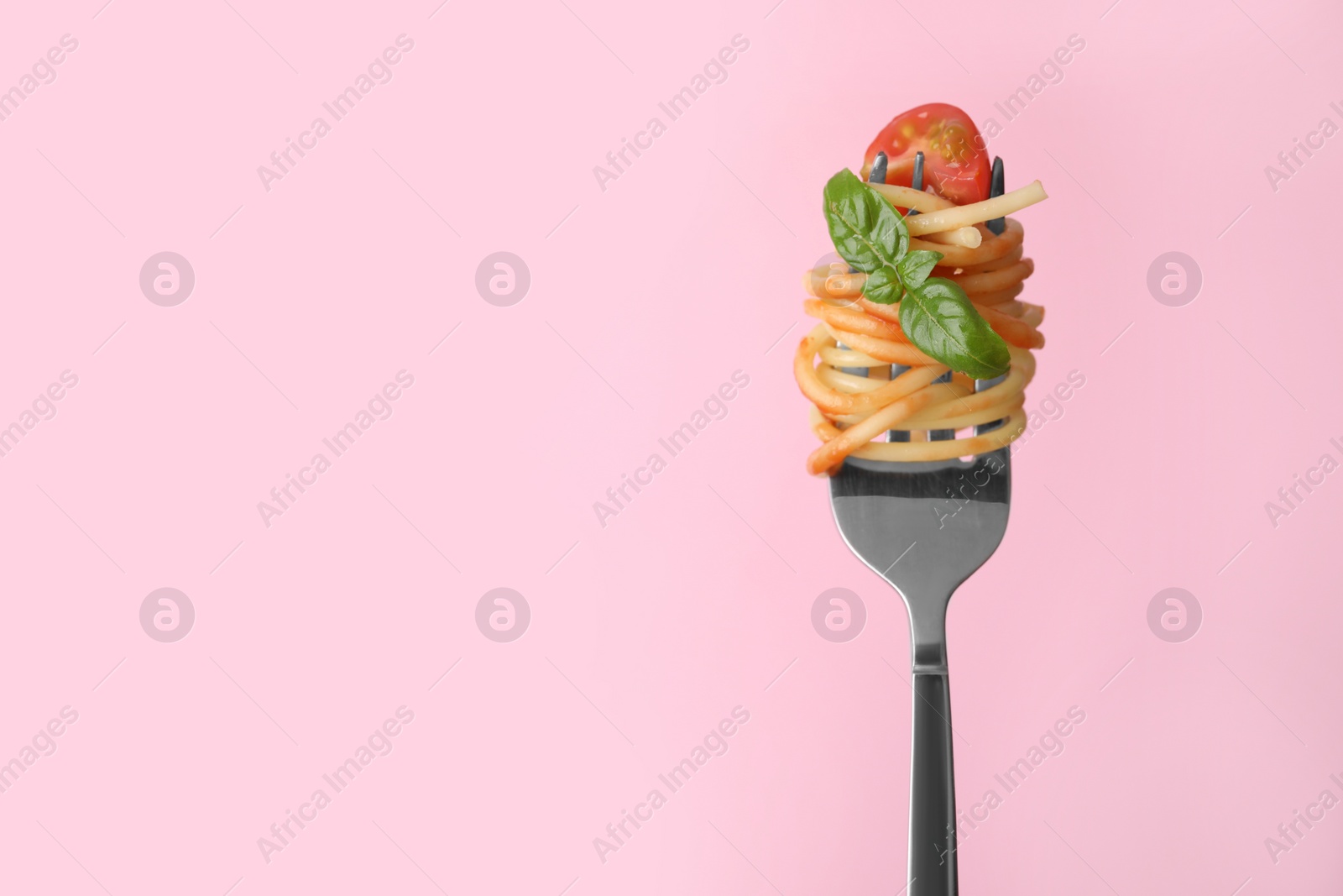 Photo of Tasty pasta with tomato sauce and basil on fork against pink background, space for text