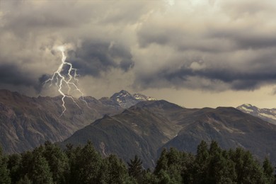 Dark cloudy sky with lightnings over beautiful trees and mountains. Thunderstorm