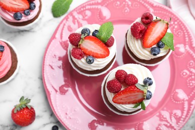 Photo of Delicious cupcakes with cream and berries on white marble table, flat lay