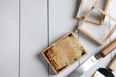 Honeycomb frame and beekeeping tools on white wooden table, flat lay. Space for text