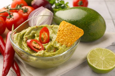 Photo of Bowl of delicious guacamole, nachos chip and ingredients on table, closeup