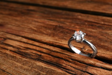 Photo of Beautiful luxury engagement ring with gemstone on wooden background, closeup. Space for text