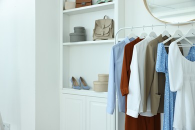 Photo of Rack with different clothes near shelving unit with shoes and bags indoors