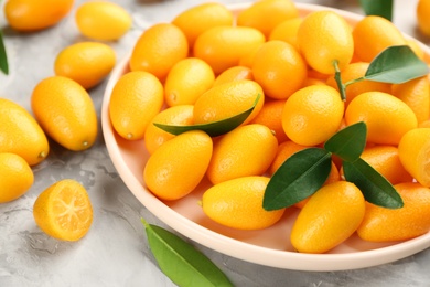 Photo of Fresh ripe kumquats in plate on light grey table, closeup