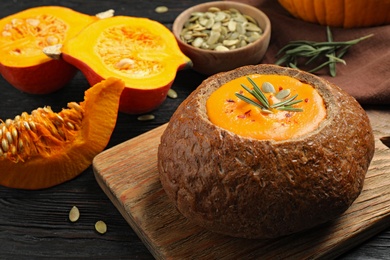 Photo of Tasty pumpkin cream soup in bread loaf on wooden table