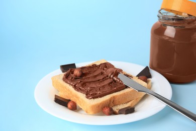 Photo of Tasty toast with chocolate paste and nuts near jar of cream on light blue background