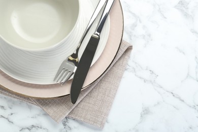 Photo of Clean plates, bowl, cutlery and napkin on white marble table, top view. Space for text