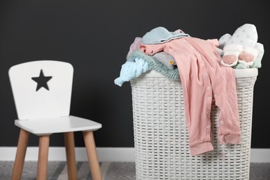 Photo of Laundry basket with baby clothes and white wooden chair indoors