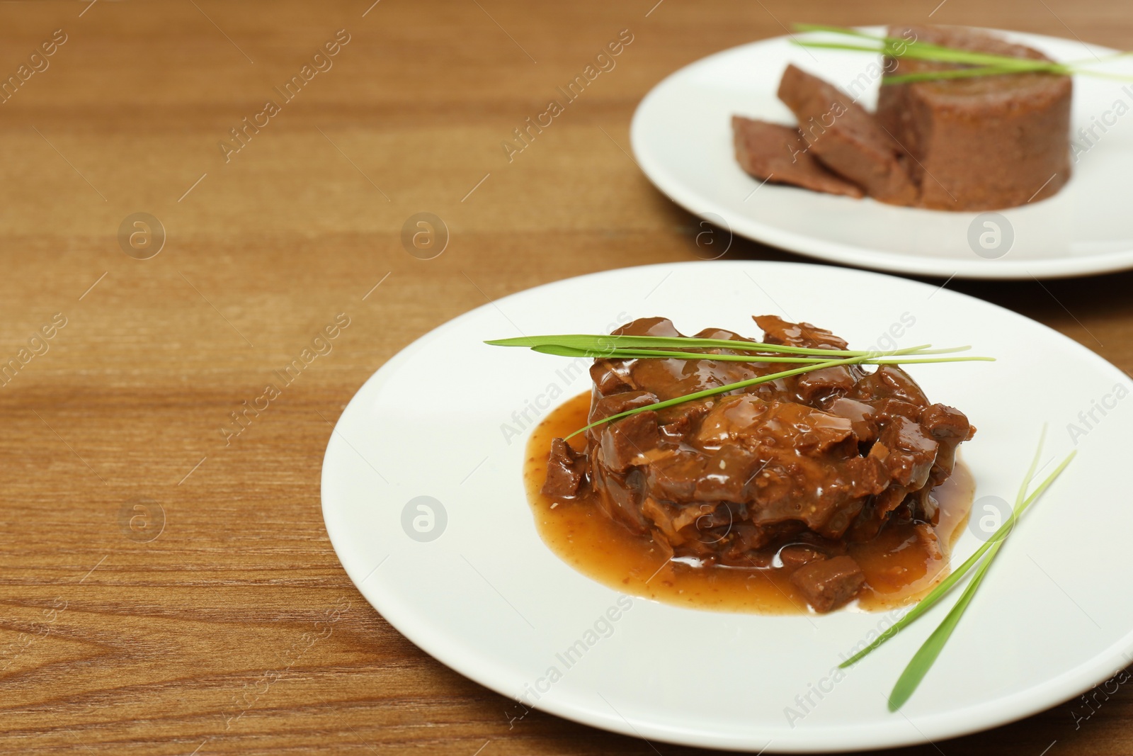 Photo of Plate with wet pet food and grass on wooden table, space for text