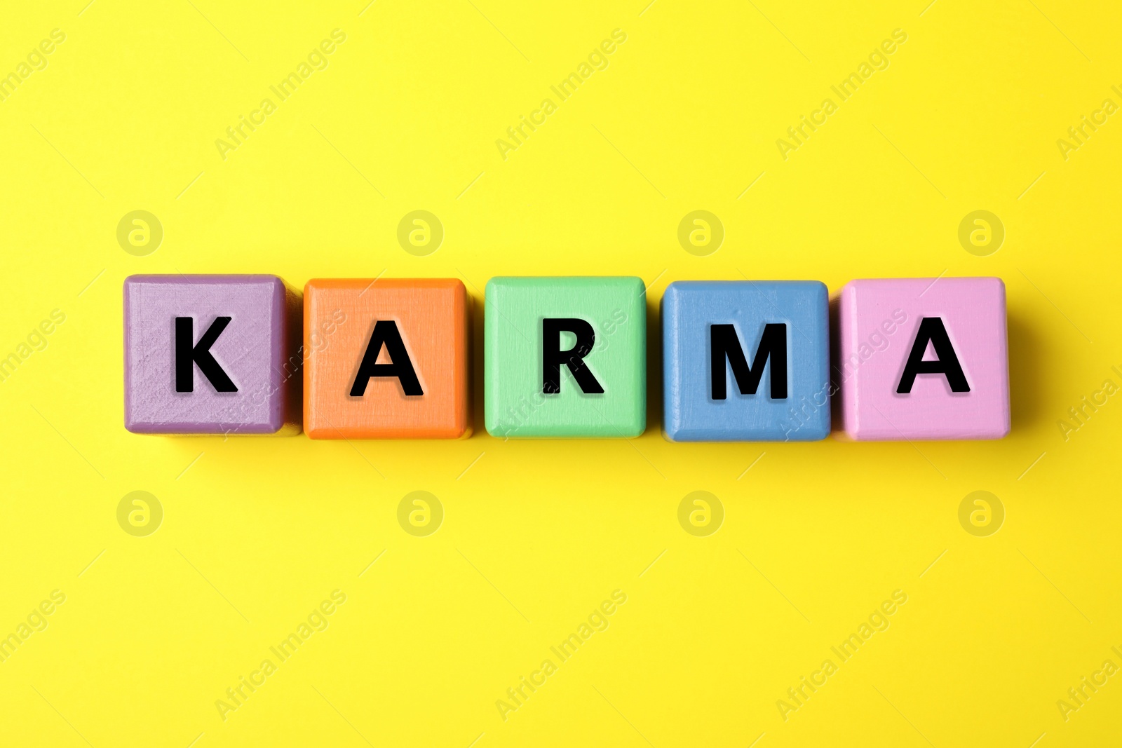 Photo of Word Karma made of colorful cubes with letters on yellow background, top view