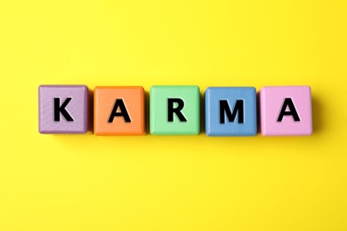 Word Karma made of colorful cubes with letters on yellow background, top view