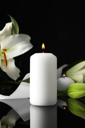 Photo of White lilies and burning candle on black mirror surface in darkness, space for text. Funeral symbols