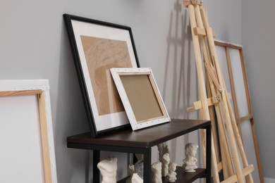 Photo of Wooden easel near shelving unit with canvases and small sculptures in artist's studio