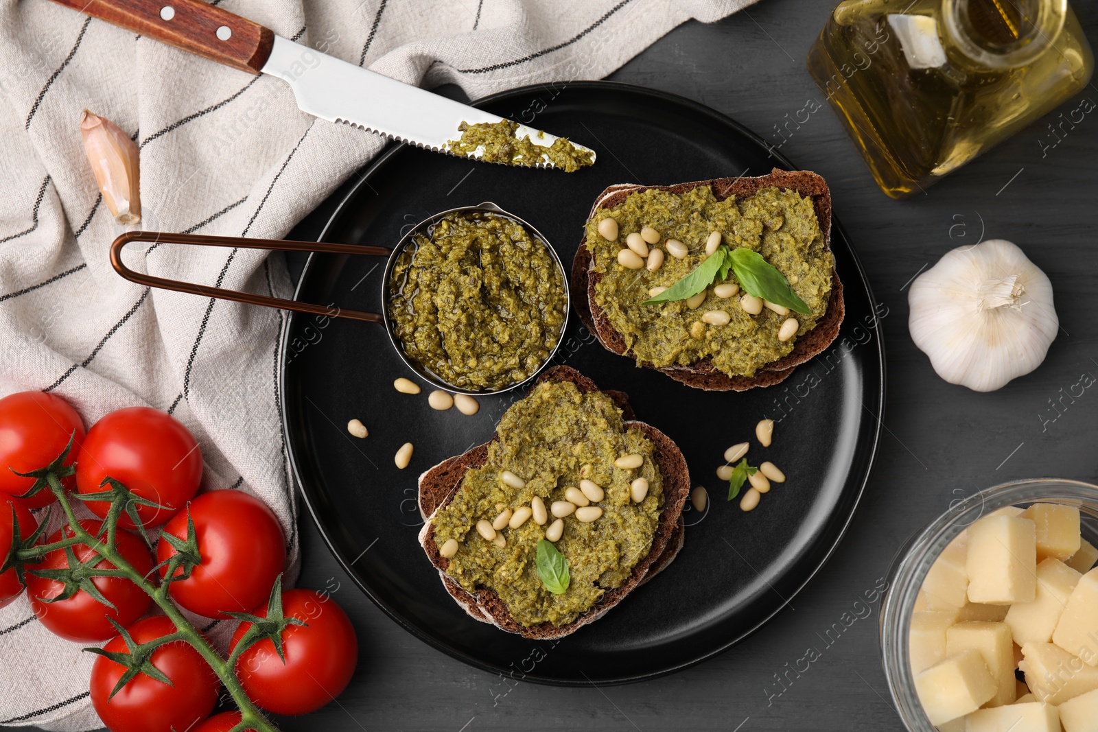 Photo of Tasty bruschettas with pesto sauce and ingredients on dark grey table, flat lay