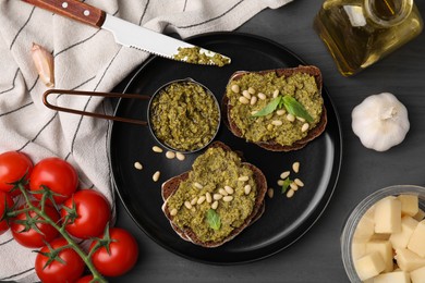 Photo of Tasty bruschettas with pesto sauce and ingredients on dark grey table, flat lay