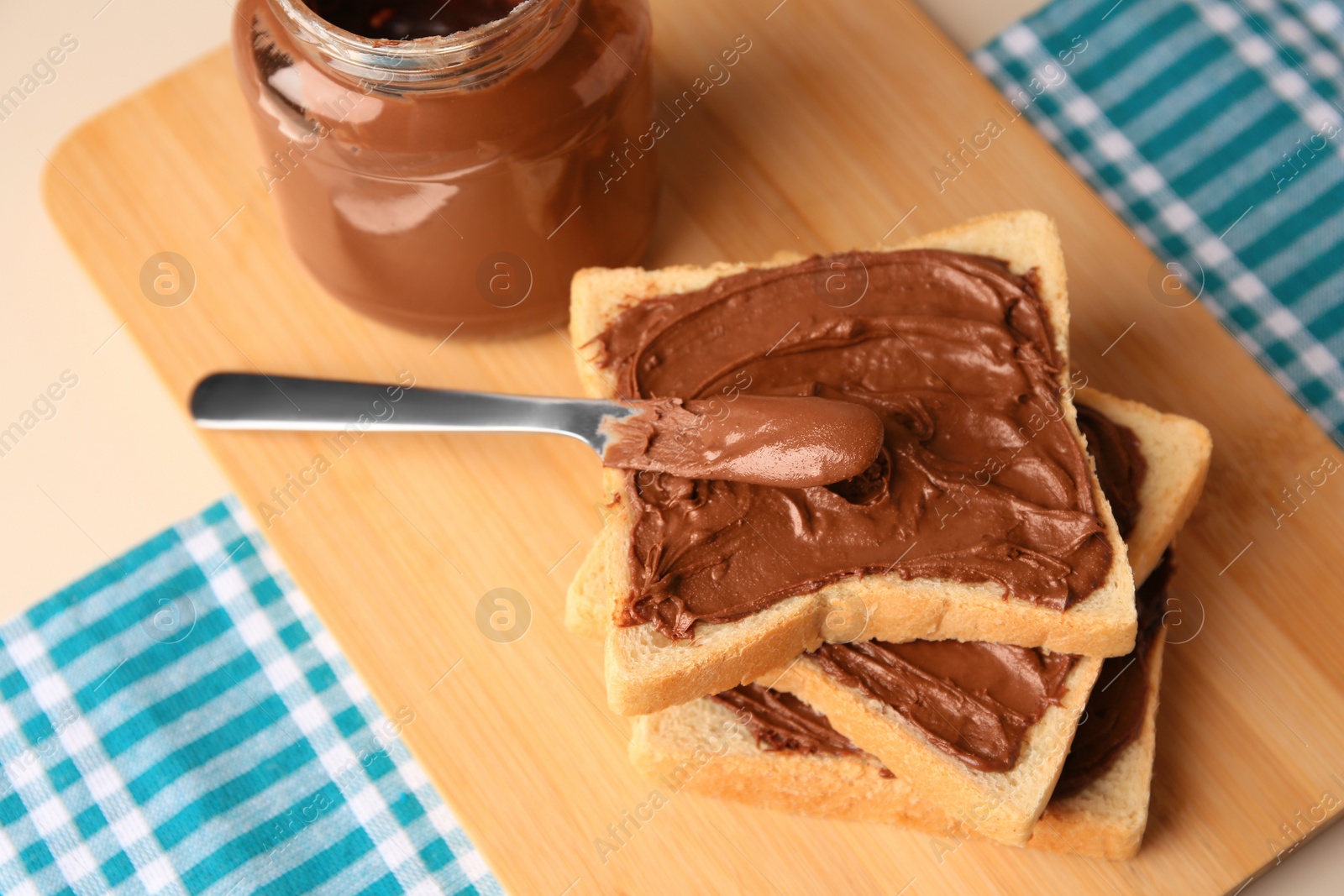 Photo of Tasty toasts with chocolate paste and jar of cream on beige table