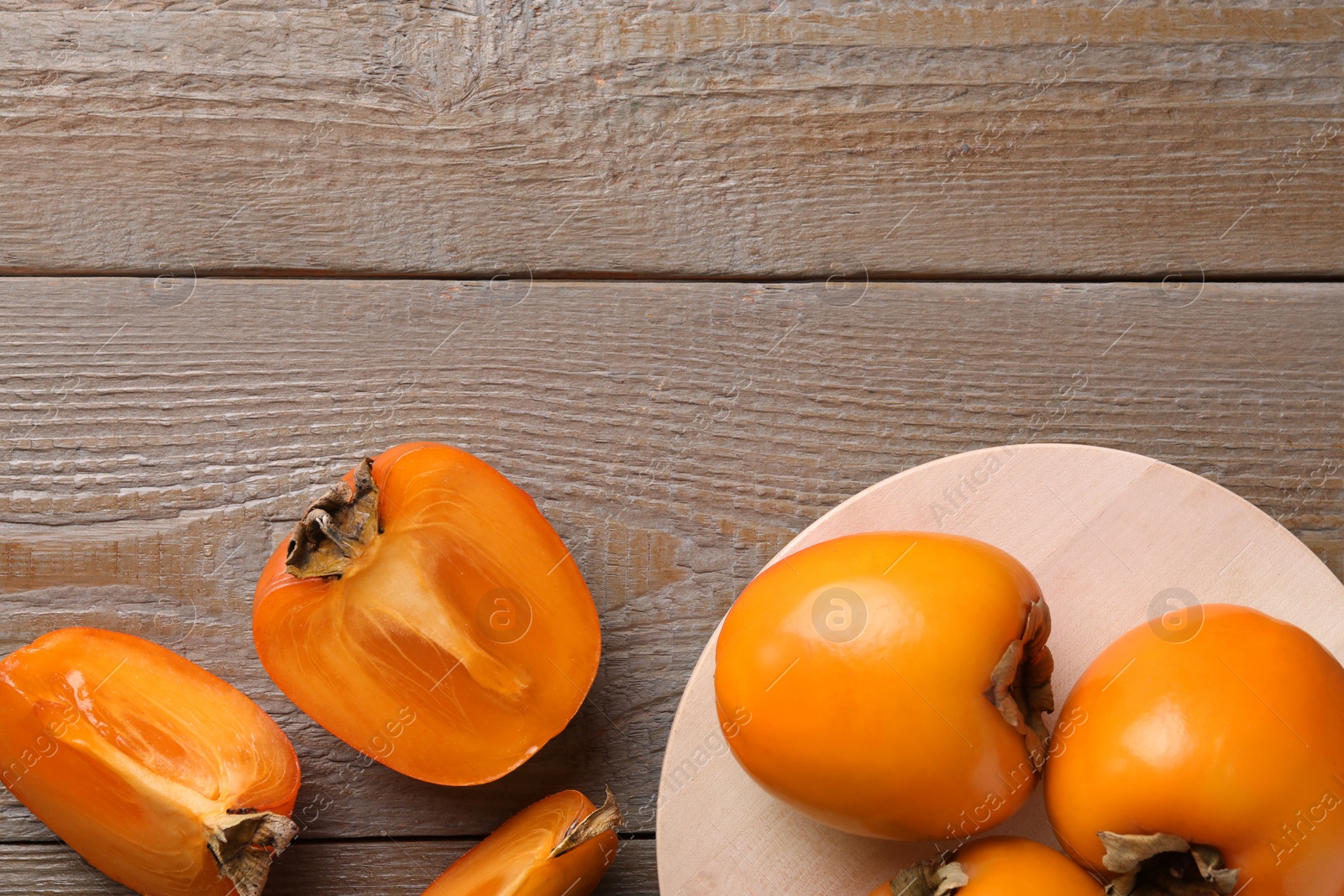 Photo of Whole and cut delicious ripe persimmons on wooden table, flat lay. Space for text