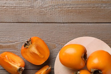 Photo of Whole and cut delicious ripe persimmons on wooden table, flat lay. Space for text