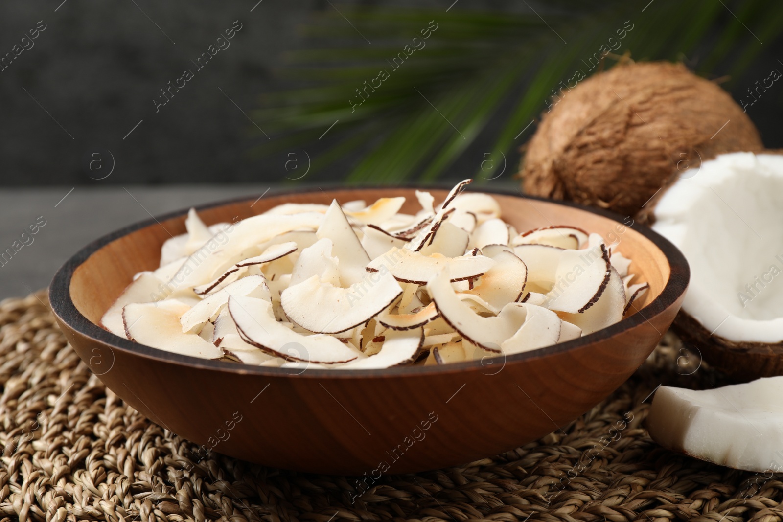 Photo of Tasty coconut chips in bowl on wicker mat