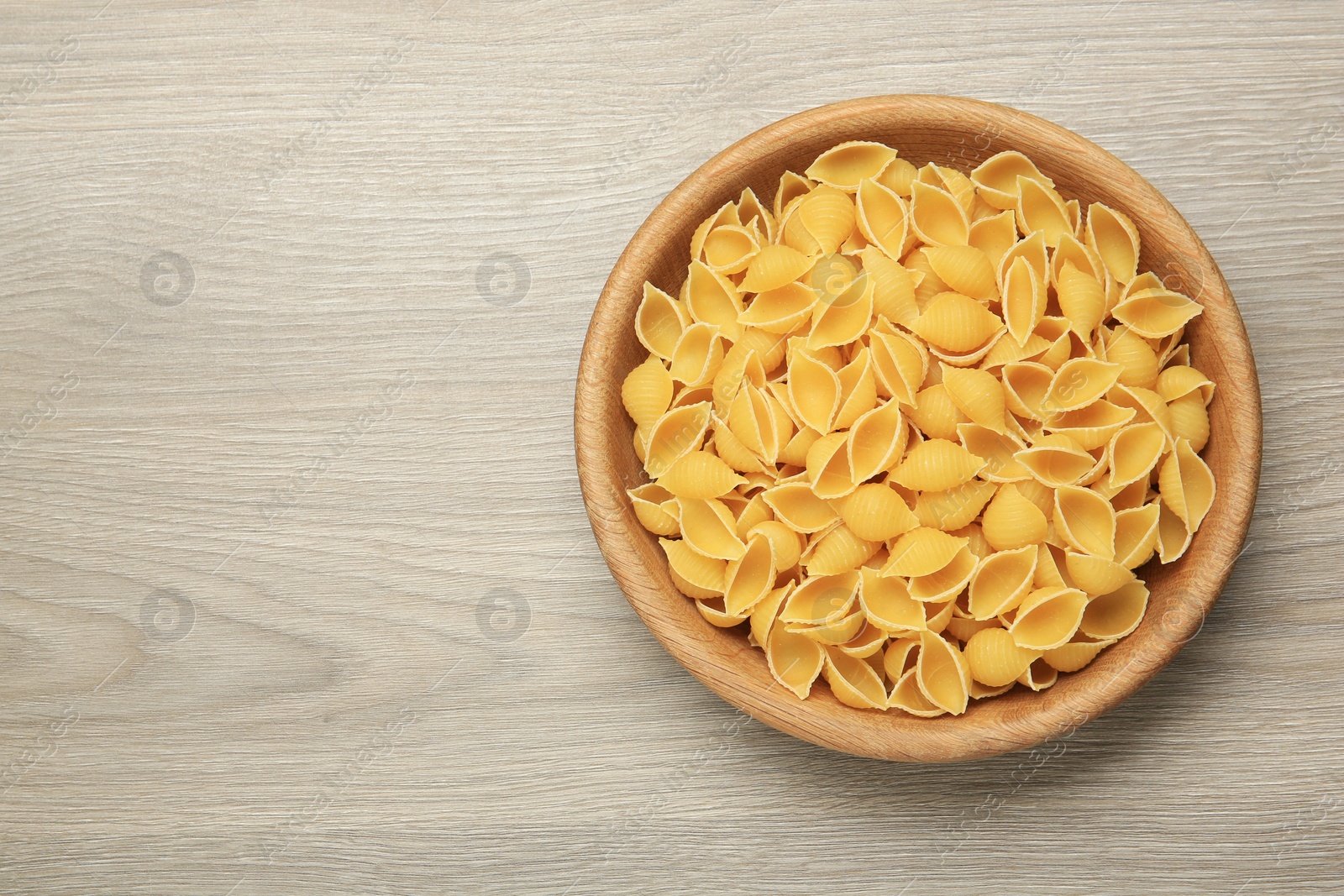 Photo of Raw conchiglie pasta in bowl on light grey wooden table, top view. Space for text