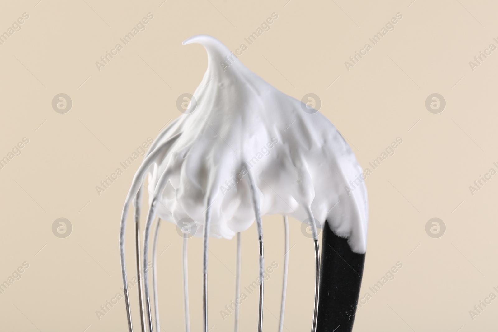 Photo of Whisk with whipped cream on beige background, closeup