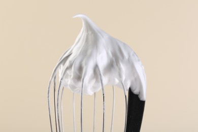 Whisk with whipped cream on beige background, closeup