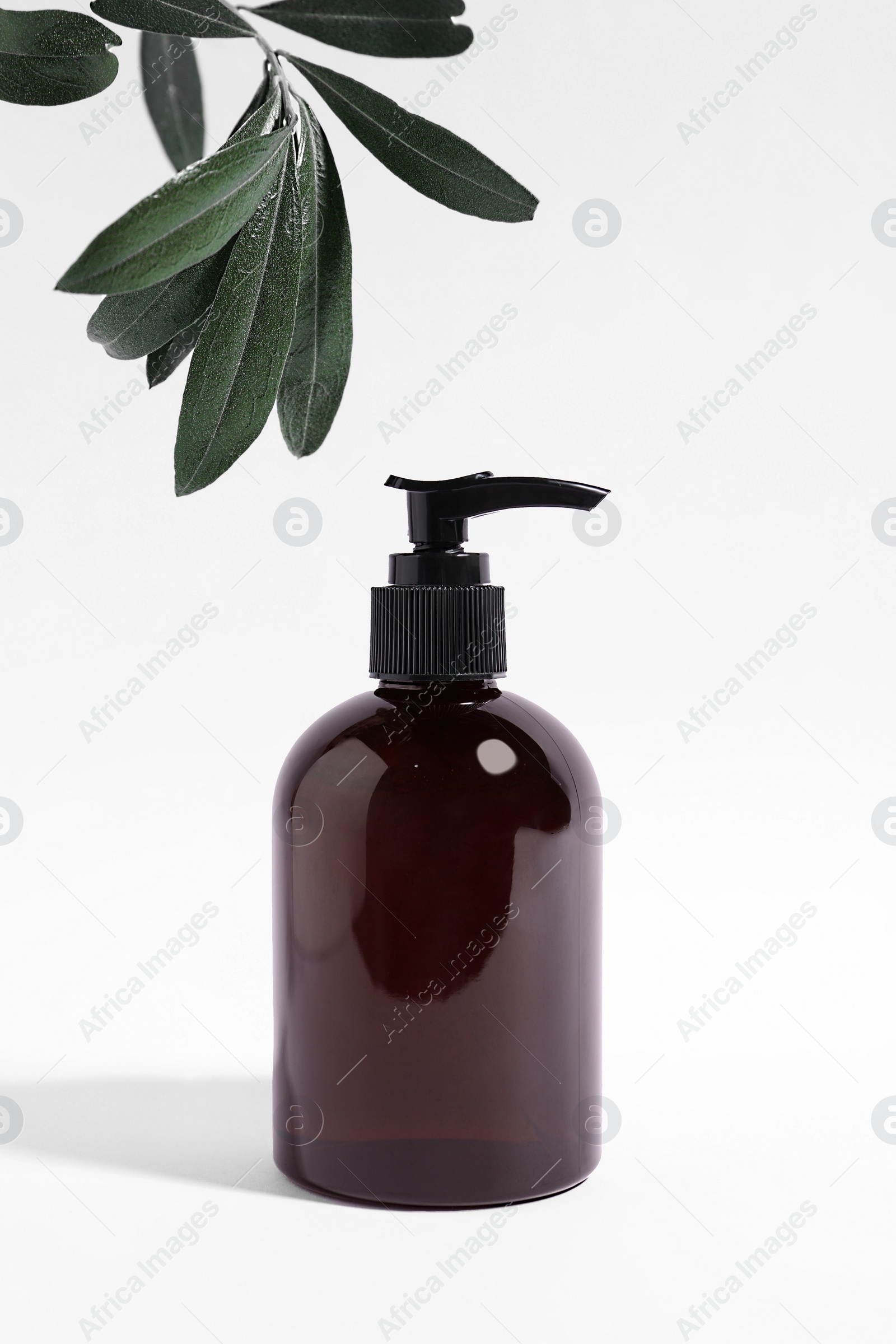 Photo of Bottle with cosmetic product and green leaves on white background