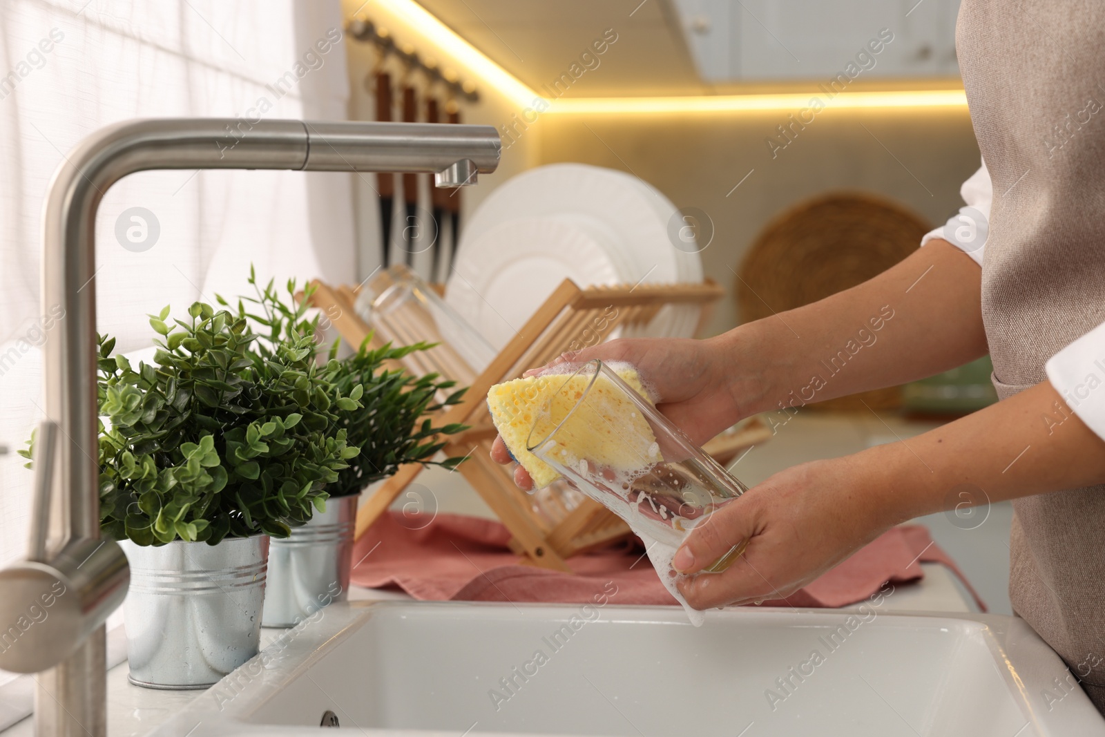 Photo of Woman washing glass at sink in kitchen, closeup