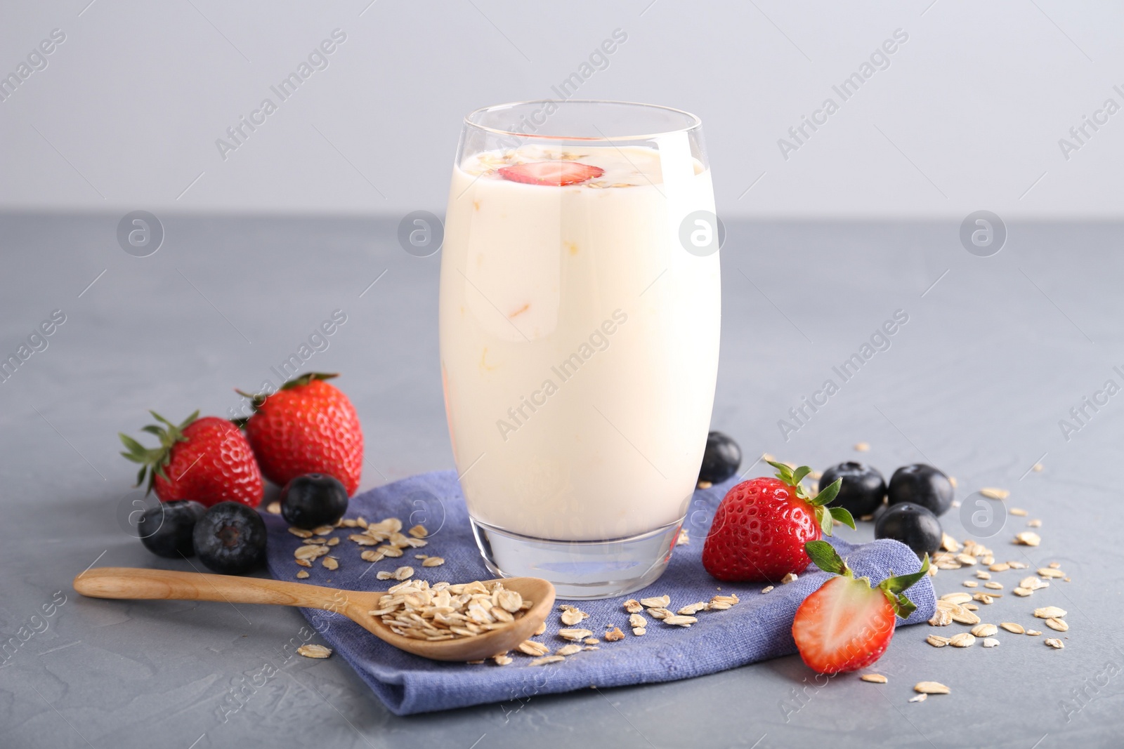 Photo of Tasty yogurt in glass, oats and berries on grey table