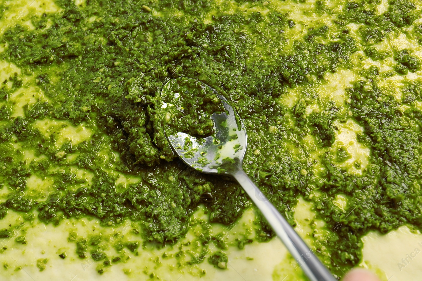 Photo of Making delicious pesto bread. Putting sauce onto raw dough, closeup