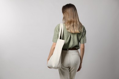 Woman with eco friendly bag on light background, back view