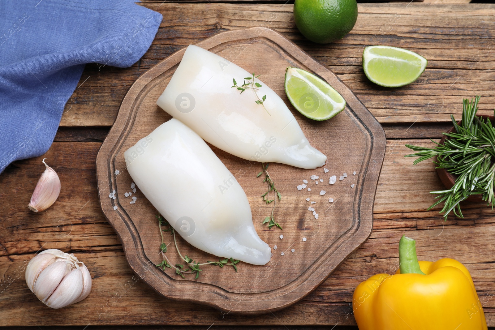 Photo of Flat lay composition with fresh raw squid tubes and garnish ingredients on wooden table