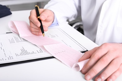 Doctor examining cardiogram at table in clinic, closeup