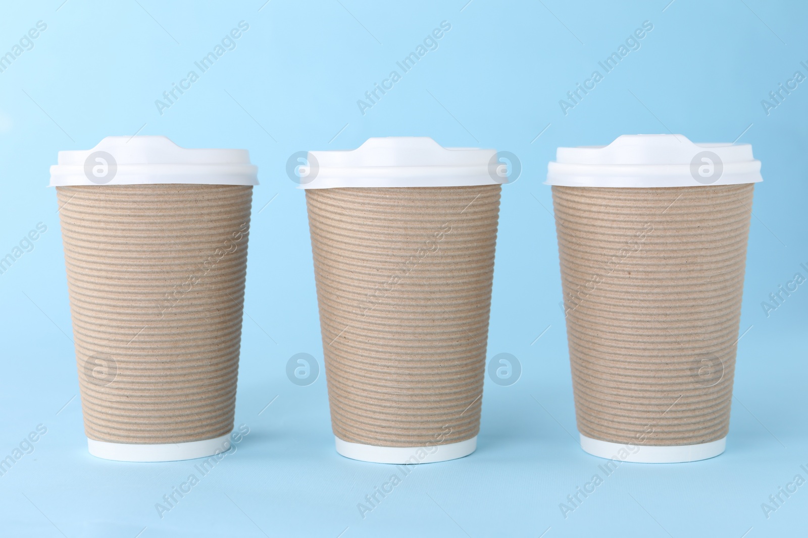 Photo of Paper cups with white lids on light blue background. Coffee to go