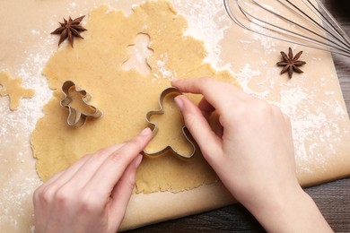 Woman making Christmas cookies with cutters at wooden table, top view