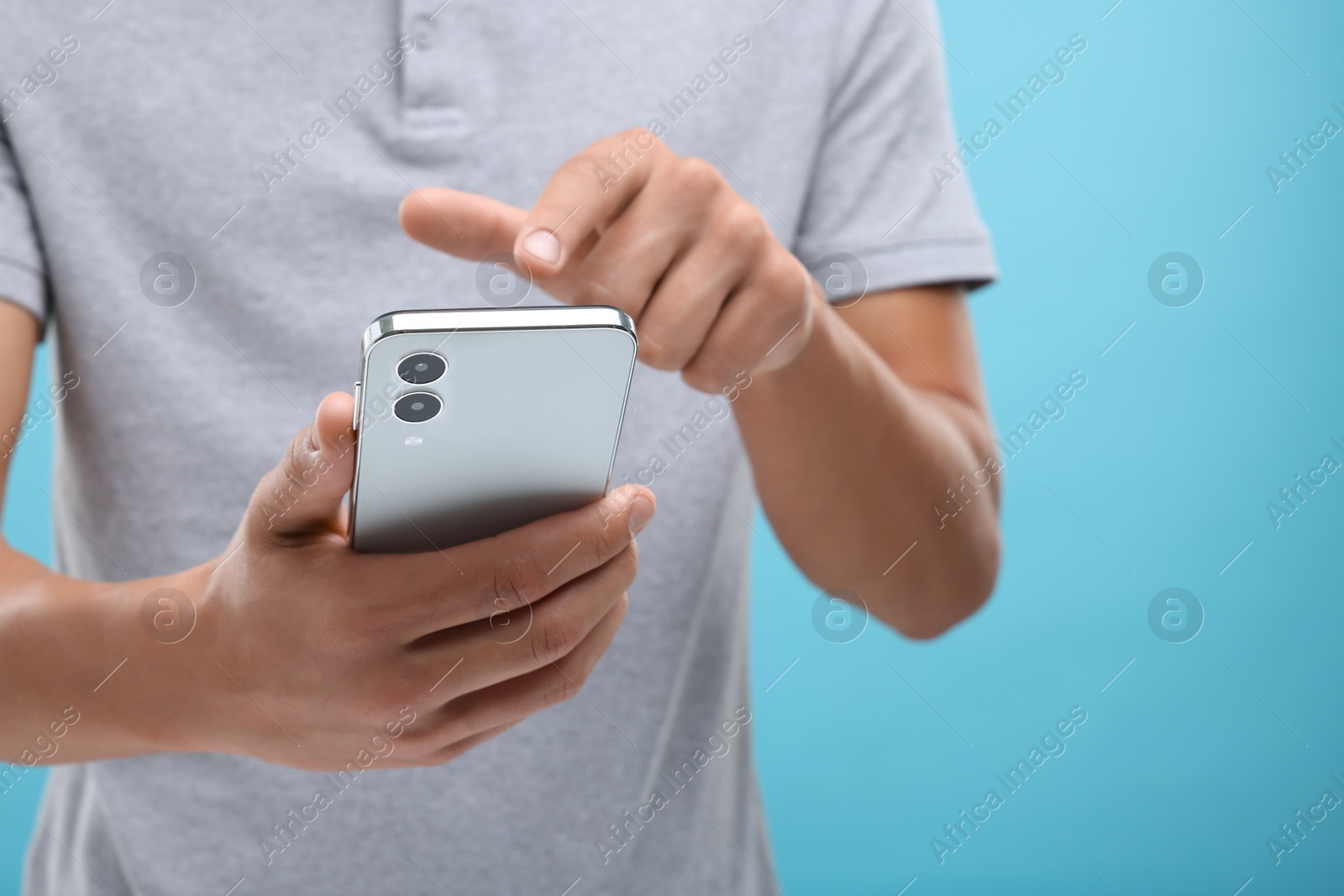 Photo of Young man sending message via smartphone on light blue background, closeup