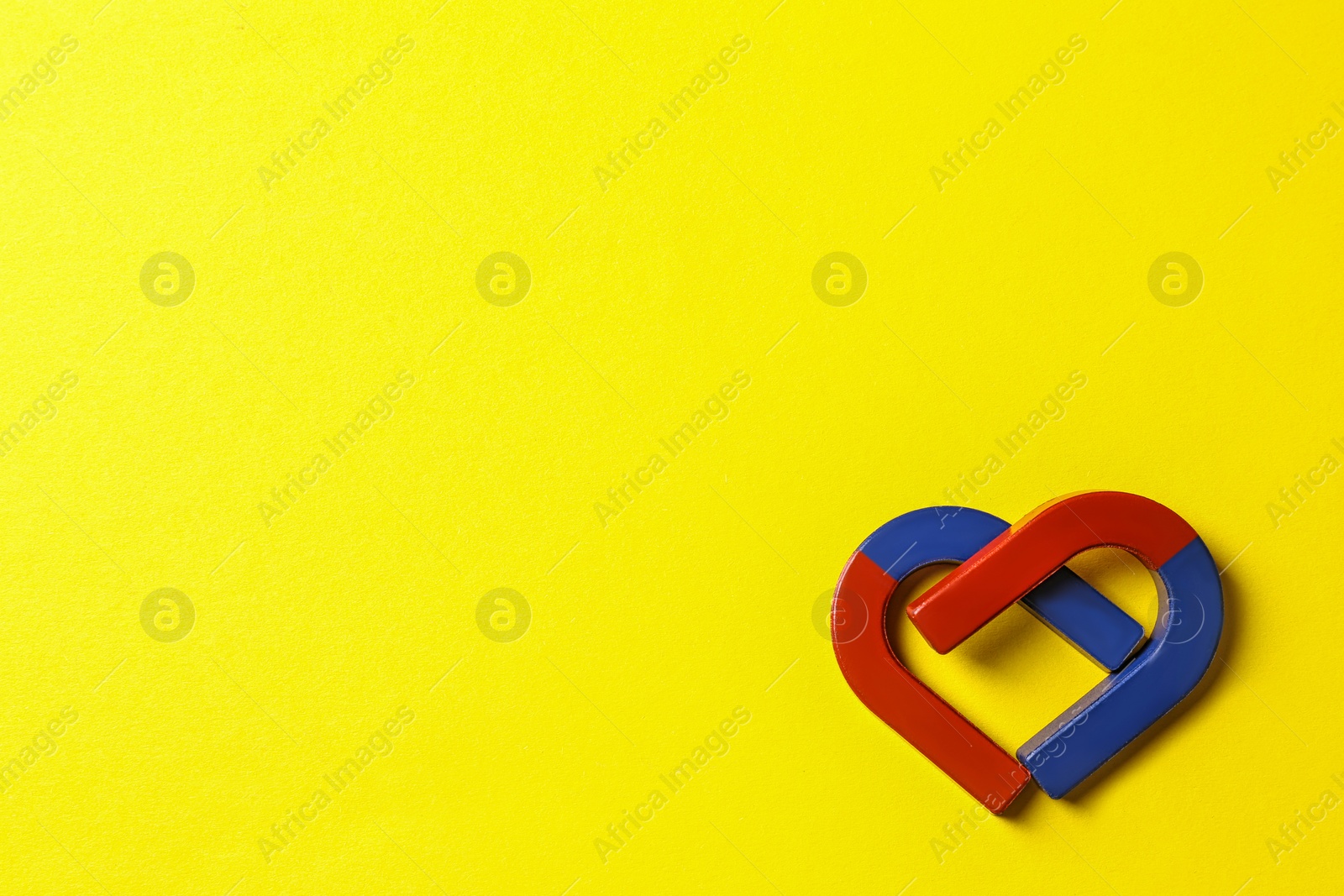 Photo of Red and blue horseshoe magnets on yellow background, flat lay. Space for text