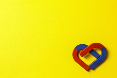 Photo of Red and blue horseshoe magnets on yellow background, flat lay. Space for text