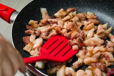 Woman cooking cracklings in frying pan, closeup. Pork lard