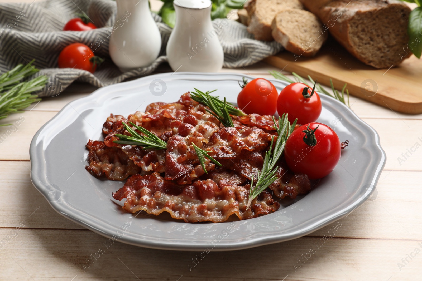 Photo of Slices of tasty fried bacon with rosemary and tomatoes served on wooden table