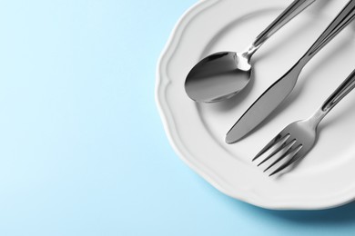 Photo of Stylish silver cutlery and plate on light blue background, top view. Space for text