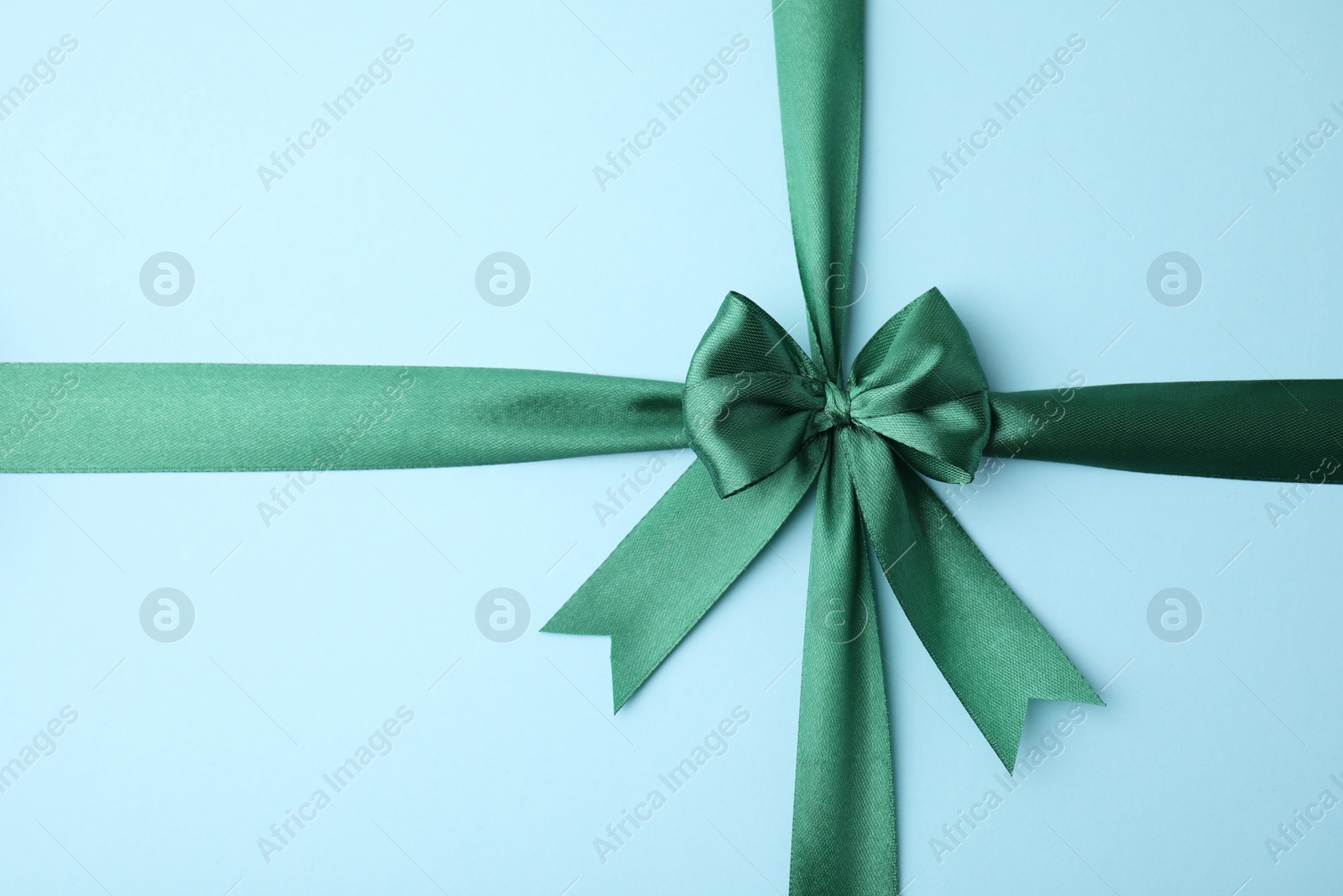 Photo of Green satin ribbon with bow on light blue background, top view