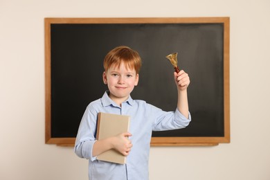 Photo of Cute little boy ringing school bell in classroom