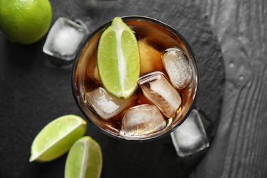 Photo of Glass of cocktail with cola, ice and cut lime on table, flat lay