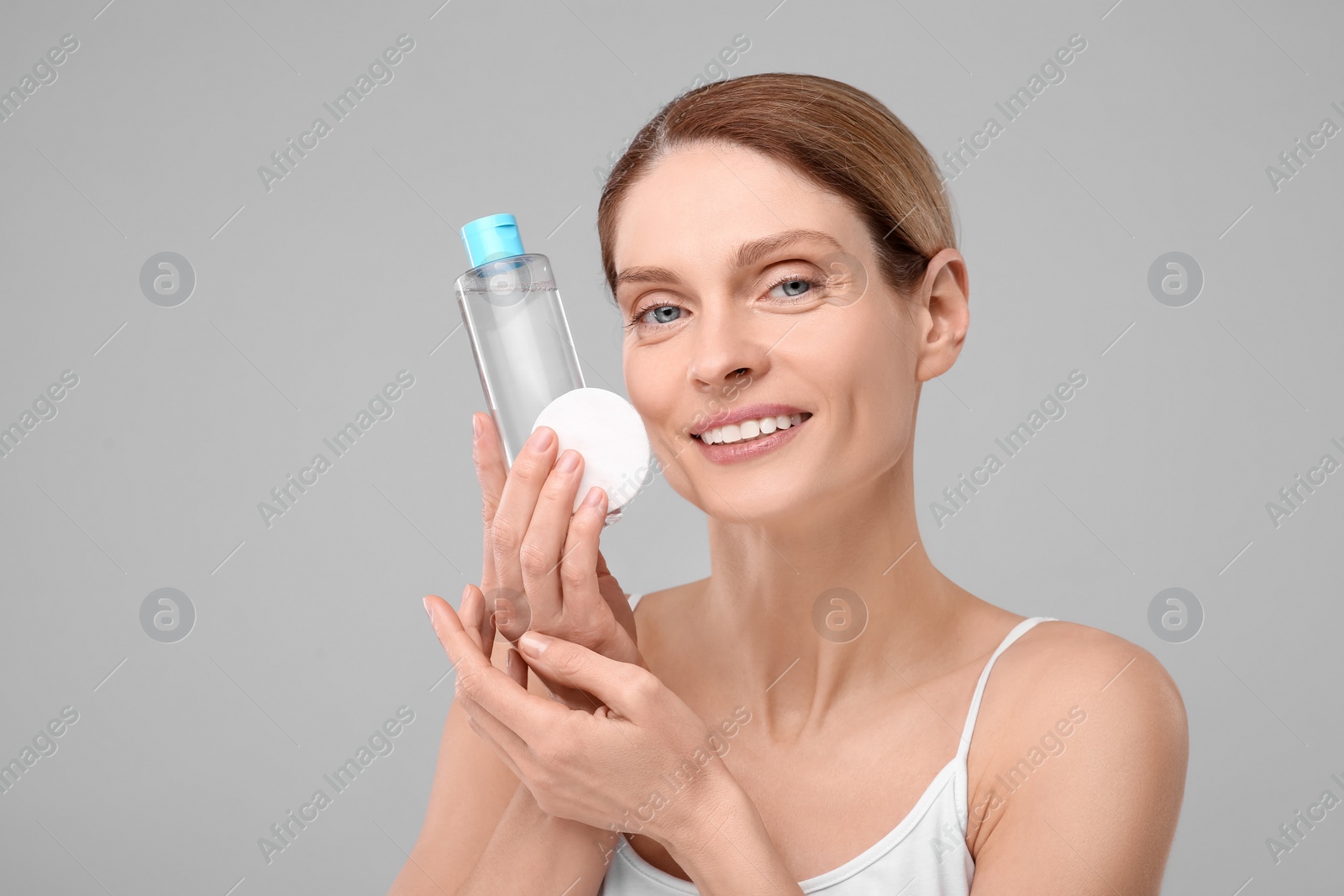 Photo of Beautiful woman with makeup remover and cotton pad on gray background, space for text