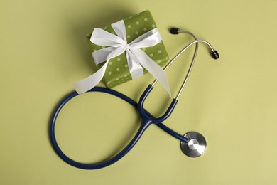 Photo of Stethoscope and gift box on green background, flat lay. Happy Doctor's Day